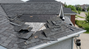 Wind damage to a roof with several shingles blown off or lifted exposing underlayment